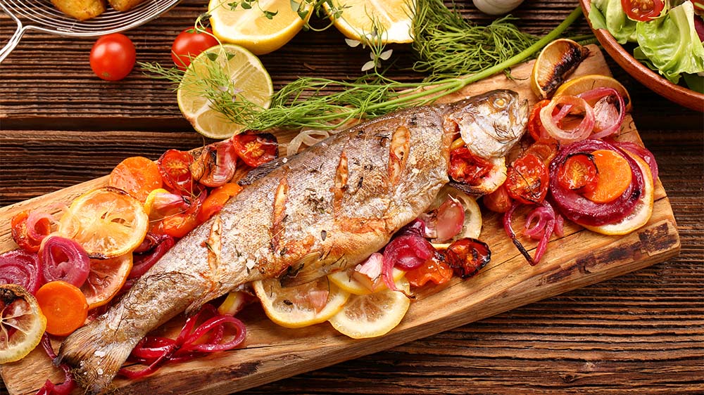 Fisch grillen: Fisch mit Gemüse und Kartoffeln auf Holz