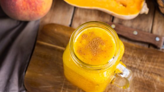 Healthy raw pumpkin butternut squash smoothie with peaches, bananas, nuts in glass mason jar. Plank wood table, rustic kitchen interior, kinfolk style. Top view.