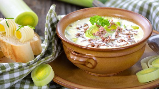 Creamy cheese and leek soup with minced meat, served with buttered baguette on a wooden table
