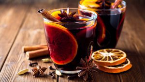 Zwei Gläser mit Glühwein und Orangen im Glas. Dazu Zimtstangen und Sternanis auf einem Holztisch