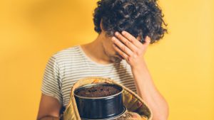 An upset young man is holding a burnt cake