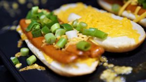 Sandwich: Käse Hot Dog liegt auf der Bratplatte und wird mit Lauchzwiebeln garniert.