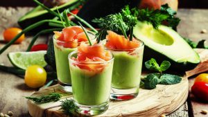 Brunch-Ideen: 3 gläser mit Avocado-Crème befüllt, mit Lachs garniert. Im Hintergrund grünes Gemüse und Avocado