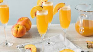 Brunch-Ideen: 3 Sektgläser gefüllt mit Bellini Cocktail. Drumherum Pfirsiche und Pfirischscheiben.