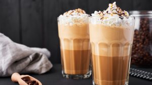 Iced caramel latte coffee in a tall glass with chocolate syrup and whipped cream. Latte Go: Dark wooden background.