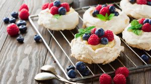 Meringues Pavlova cakes with fresh raspberry and blueberry on dark rustic wooden background, selective focus