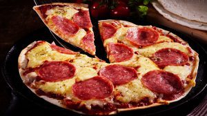 schnelle Gerichte, Slice salami and cheese tortilla pizza being served in a rustic kitchen with a closeup view on the whole pizza on an old plate