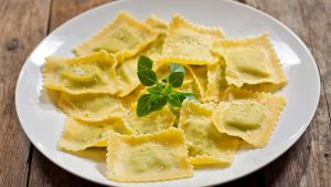 plate of ravioli with basil on wooden table