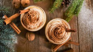 top view of delicious eggnog drink near spruce branches, wallnuts and cinnamon sticks on wooden table