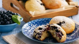 Quarkbrötchen mit Blaubeeren aufgebrochen auf einem Teller mit einer Tasse Kaffee auf dem Tisch