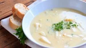 Spargelsuppe auf einem Teller mit Baguettescheiben