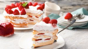 Stück Erdbeertorte auf einem Teller, im Hintergrund gedeckte Kaffeetafel
