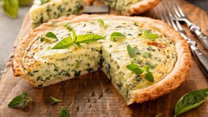 Quiche mit Kräutern und Spinat auf Holzbrett