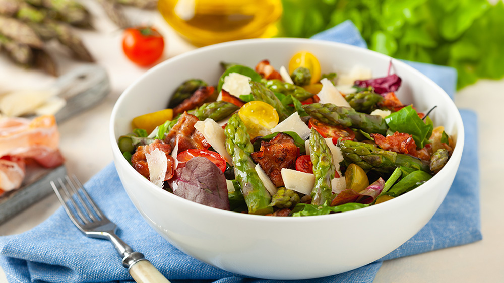Grüner Spargelsalat mit Tomaten, Spinat und Parmesan in einer Bowl.