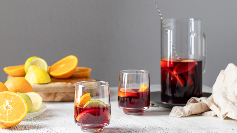 Zwei Gläser und eine Karaffe mit Tinto de Verano sowie Orangen- und Limettenscheiben stehen auf einem Tisch.