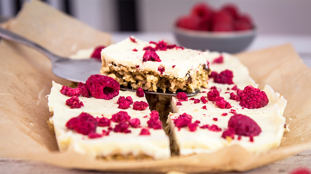 Ein Flapjack-Riegel mit weißer Schokolade und Himbeeren liegt auf weiteren Flapjacks