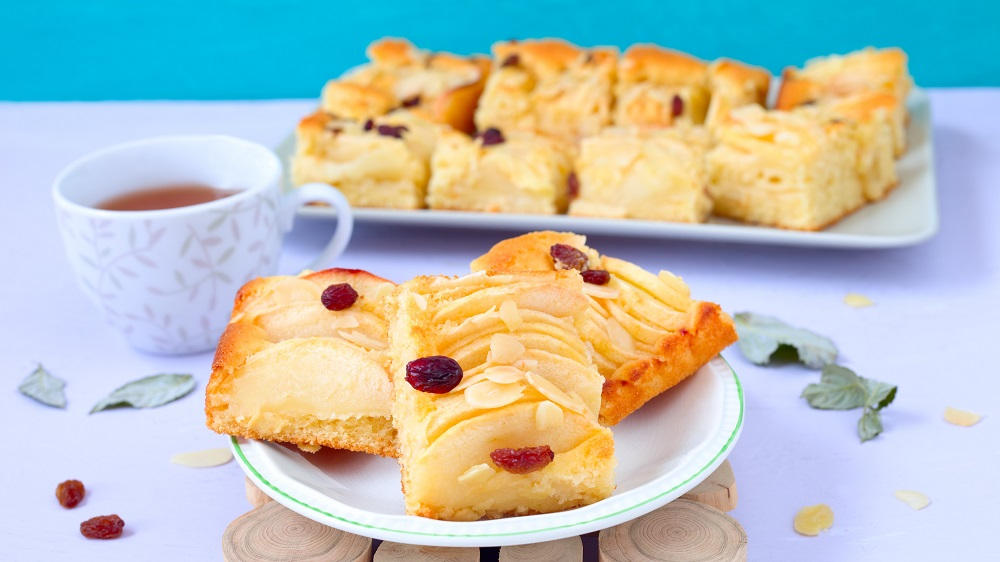 Stücke eines Apfelkuchen vom Blech auf Teller.