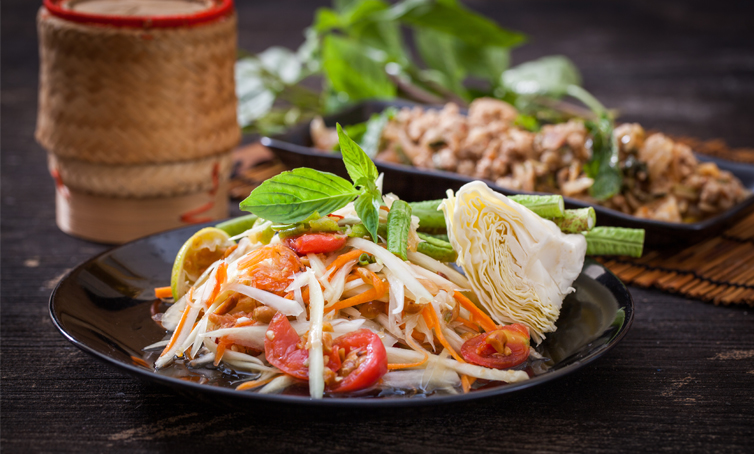 Thailändischer Papaya-Salat Tom Sam ist auf einem schwarzen Teller angerichtet.