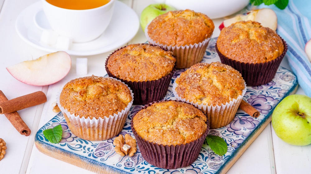 Apfel-Zimt-Muffins in Förmchen auf einem Brett.