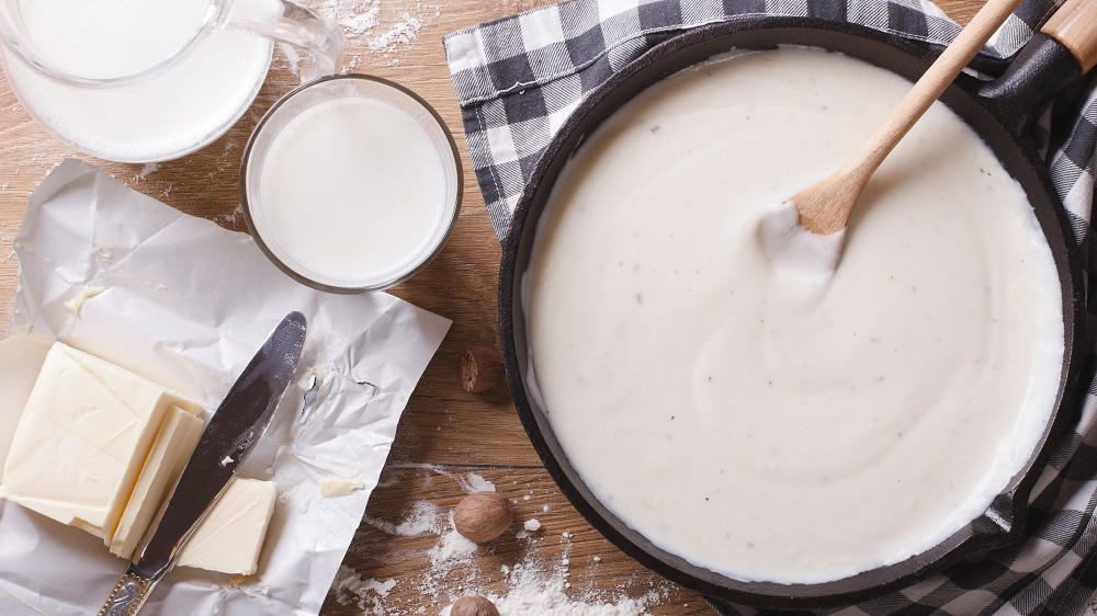 Béchamelsoße in einer Pfanne mit Kochlöffel und Zutaten.