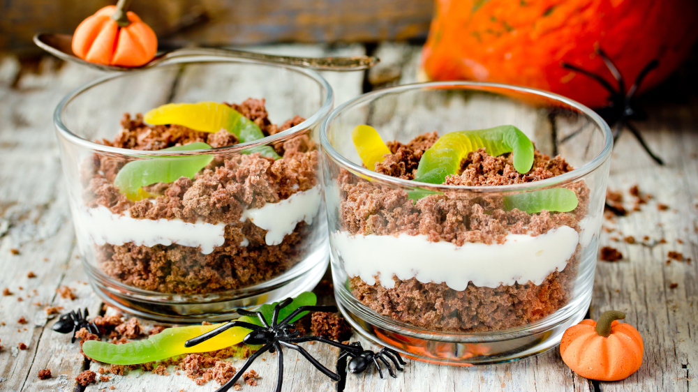 Zwei geschichtete Halloween-Desserts im Glas mit Gummiwürmern und Spinnen-Deko.