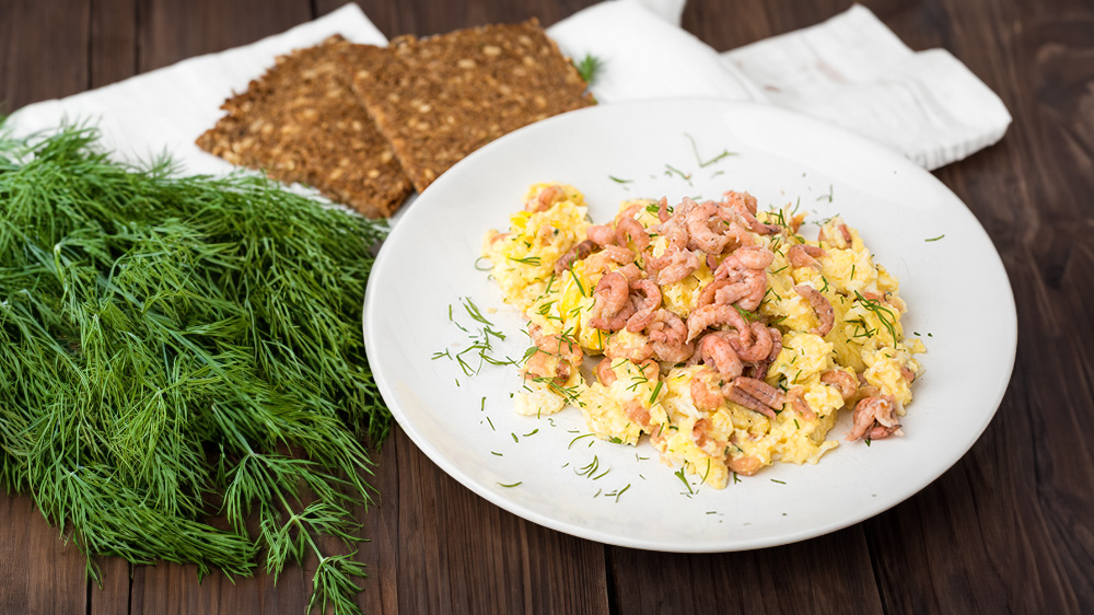 Nordseekrabben mit Rührei und Brot auf einem Teller.