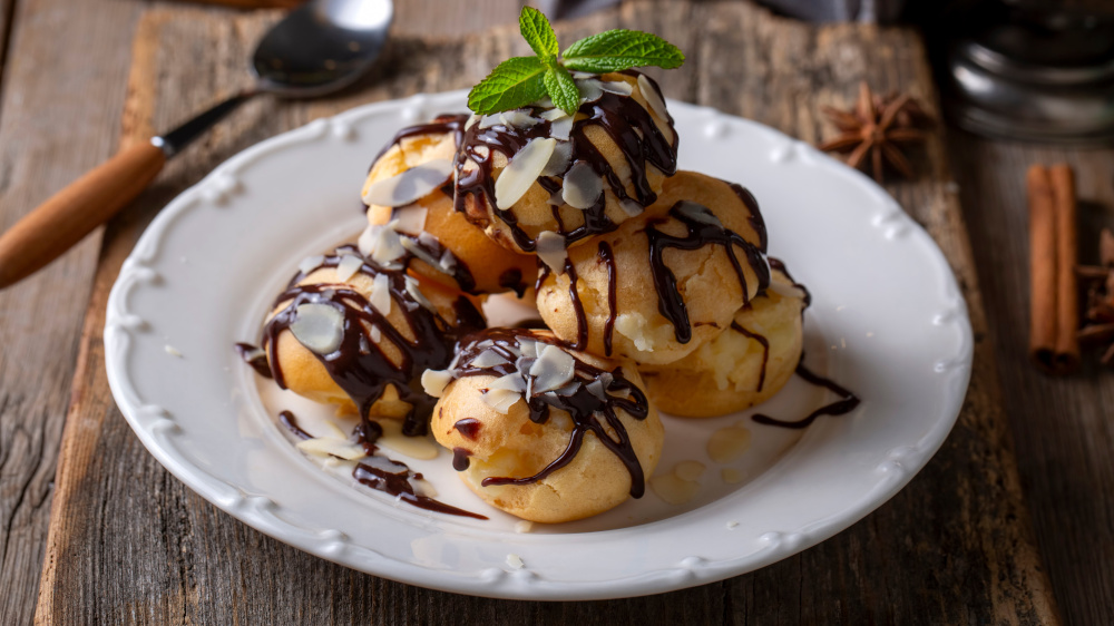 Profiteroles mit Schokosoße liegen auf einem Teller.