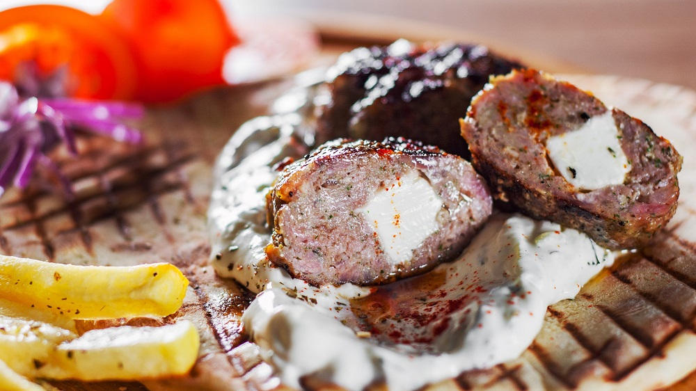 Bifteki mit Taztiki und Pommes auf einem Pita-Brot.